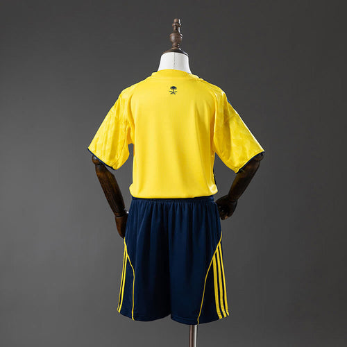 Al Nassr Kids Home 25/26 — back view of yellow shirt with Saudi crest and navy shorts