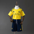 Al Nassr Kids Home 25/26 — front view, yellow shirt with KAFD sponsor, Al Nassr crest and navy shorts