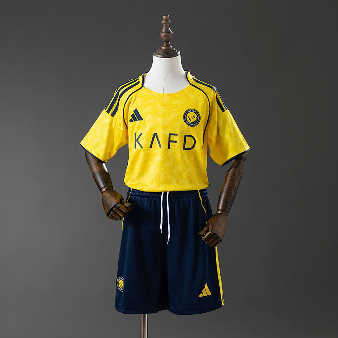 Al Nassr Kids Home 25/26 — front view, yellow shirt with KAFD sponsor, Al Nassr crest and navy shorts
